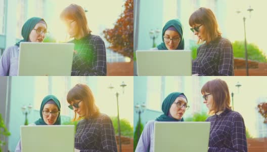 穆斯林女学生戴着头巾和眼镜，她的朋友戴着眼镜在公园里用笔记本电脑聊天，太阳耀斑。缓慢的莫高清在线视频素材下载