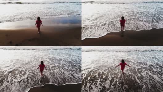 日落时分，身着红色连衣裙的女子走在海边的沙滩上，灵感自由快乐的度假理念，从无人机空中拍摄，从上方观看高清在线视频素材下载