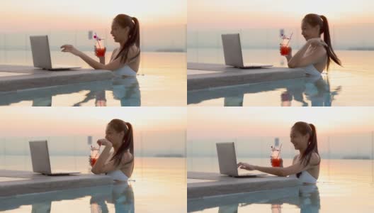 穿着比基尼的亚洲女人在泳池喝鸡尾酒，在笔记本电脑上搜索电视剧，在互联网流媒体服务上选择电影休闲在早上，晚上。模糊的背景光线，日落，日出高清在线视频素材下载