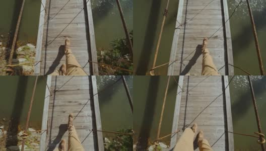 慢镜头拍摄的一名潮人走在一座木桥上，桥横跨山间河流。男人的腿在休闲旅行靴子的俯视图高清在线视频素材下载