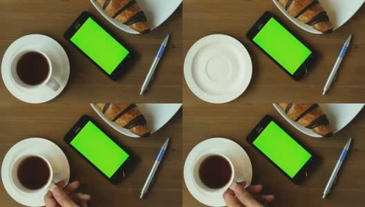 早间新闻与咖啡-咖啡杯和巧克力羊角面包在木桌子上绿色屏幕智能手机。高清在线视频素材下载