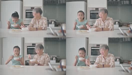 亚洲华裔孙女和她的祖母在厨房的柜台吃饺子高清在线视频素材下载