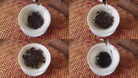 如何泡中国乌龙茶。热水从高处冲下，铁观音茶叶的颗粒在水中旋转，形成一个漩涡。茶碗里的白茶。缓慢的运动。高清在线视频素材下载
