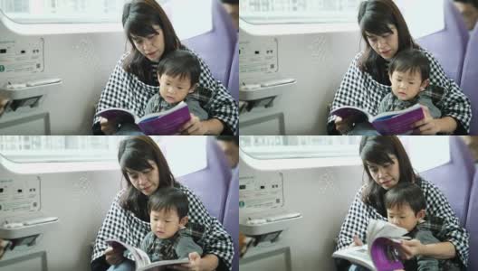 年轻的亚洲母亲和儿子在火车上看书。高清在线视频素材下载