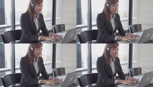 商务女性坐在办公室用耳机使用笔记本电脑工作高清在线视频素材下载