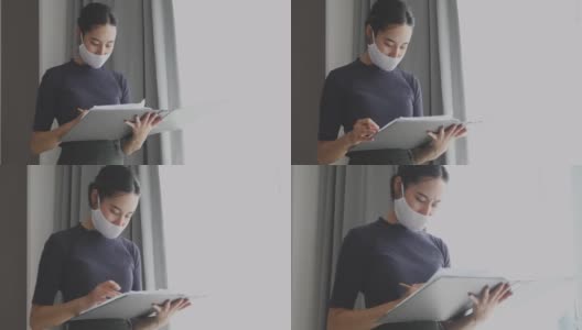 亚洲女性拿着文件，审查工作文件，在办公室戴着口罩高清在线视频素材下载