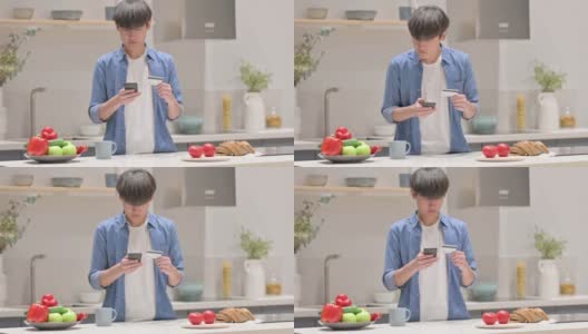 年轻的亚洲男子在厨房用智能手机在线支付高清在线视频素材下载