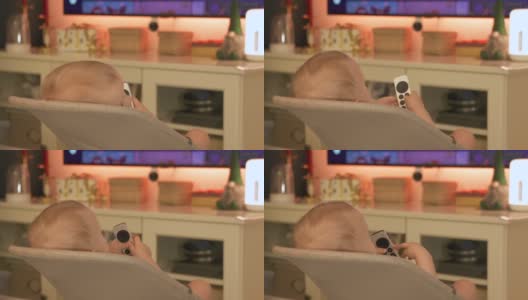白人小婴儿在家里看电视，可爱的小蹒跚学步的孩子拿着电视数字媒体播放器的遥控器。高清在线视频素材下载