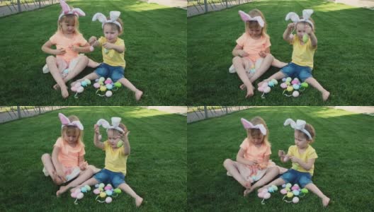 快乐的小妹妹们坐在绿色的草地上玩复活节彩蛋。高清在线视频素材下载