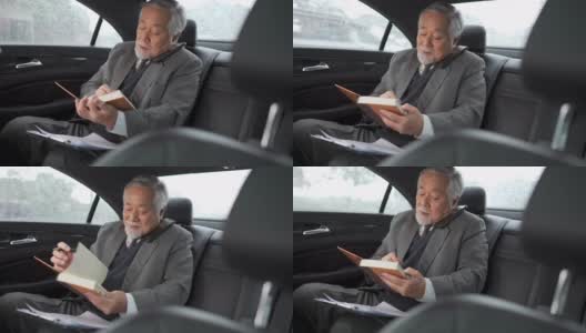4K亚洲资深商人坐在汽车后座，一边打电话一边在书中写商业计划高清在线视频素材下载