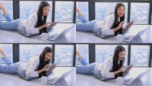 一名年轻的亚洲女性，双腿翘起，躺在地板上，在家用笔记本电脑或平板电脑观看在线数字课程，帮助员工提高技能。商学院为成人提供课程教育。高清在线视频素材下载