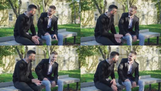 两个自信的留着胡子的年轻白人男子坐在城市公园的户外长椅上聊天。阳光明媚的周末，帅气的男性朋友在闲聊。休闲的生活方式。高清在线视频素材下载