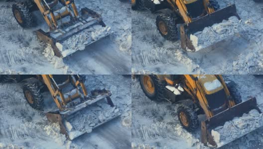 冬天的一天，一辆带着铲运机的拖拉机正在清理道路上的冰雪。道路机械正在清理积雪。市政交通、除雪机高清在线视频素材下载