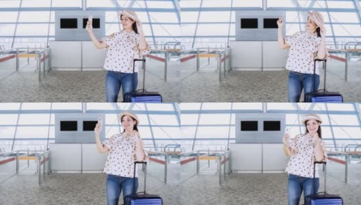快乐的年轻女子在机场候机楼拿着她的手提箱，戴着一顶帽子自拍高清在线视频素材下载