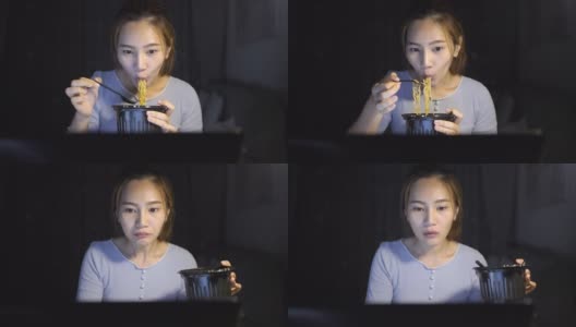 亚洲自由职业者聪明的商业妇女吃方便面，而工作在家里的客厅在笔记本电脑在晚上快乐的亚洲女孩坐在桌子上享受放松的时间高清在线视频素材下载