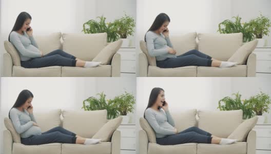 孕妇拿着手机坐在白色沙发上的4k慢动作视频。高清在线视频素材下载