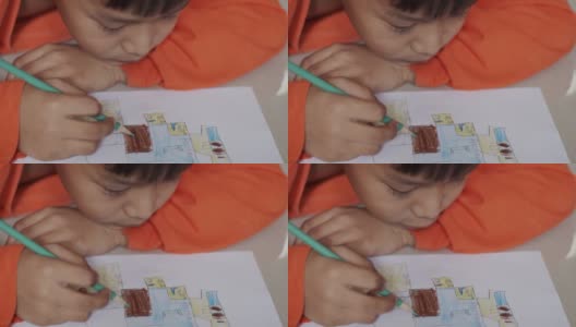 穿着橙色衬衫的小男孩正在纸上画画。高清在线视频素材下载