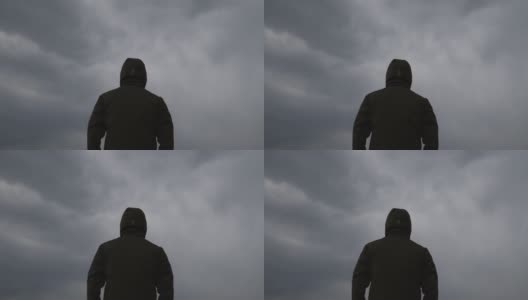 男性穿着连帽夹克的背影在天空中黑色的忧郁戏剧性的云高清在线视频素材下载