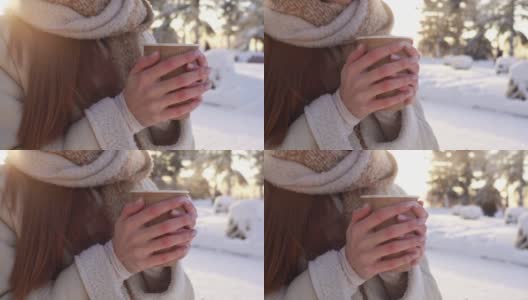 在阳光明媚的寒冷的冬天，在阳光的背景下，不认识的年轻女子的特写镜头握着杯子热气腾腾的饮料。高清在线视频素材下载