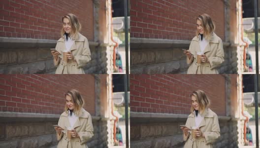 慢镜头中，一名快乐的年轻女子用智能手机走在街上，带着外带咖啡和耳机。现代科技，饮料和人的概念。高清在线视频素材下载