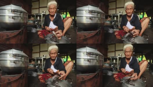 生活方式资深亚洲妇女坐在烹饪食物，慢动作高清在线视频素材下载