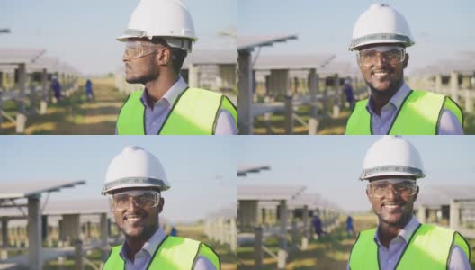 特写，肖像:在太阳能农场，非洲年轻工程师穿着防护服，戴着安全眼镜和头盔，开心地看着镜头高清在线视频素材下载