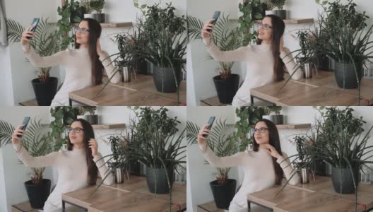 一名年轻女子戴着眼镜在咖啡馆里自拍，背景是许多植物高清在线视频素材下载