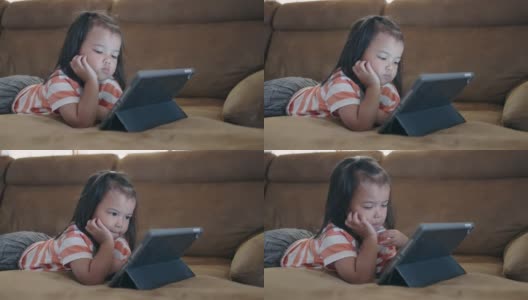 一个亚洲小女孩躺在沙发上喜欢看平板电脑高清在线视频素材下载