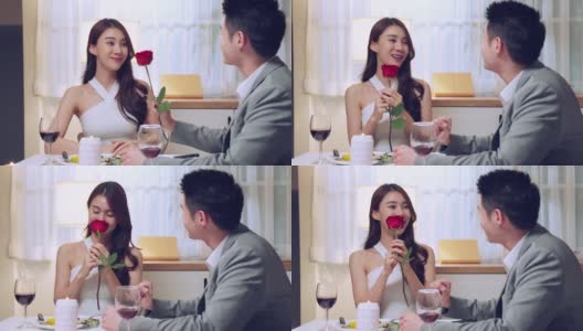 亚洲青年惊喜送玫瑰给美丽的女友。迷人浪漫的新婚夫妇，男人和女人一起吃晚餐，庆祝周年纪念日和情人节在家里高清在线视频素材下载