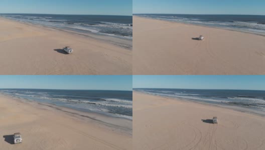 无人机航拍到的白色吉普车在非洲纳米比亚骨架海岸的沙滩上行驶。站在吉普车上看着大海的冒险家和背包客。棕色的沙子和海浪。无人机跟着货车和吉普车。高清在线视频素材下载