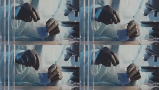 一名戴着防护橡胶手套的实验室助理在实验室设备的背景下搅拌一个烧瓶中的蓝色液体。制药行业。研究工作。高清在线视频素材下载