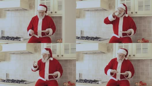圣诞老人坐在厨房家具上，吃着加牛奶的饼干高清在线视频素材下载