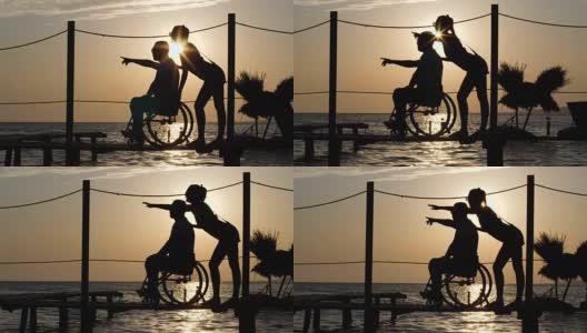 幸运的残疾人和女朋友看向远方，并显示他的手臂在背景日落在海上地平线高清在线视频素材下载