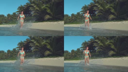 慢镜头:女子在浅海中奔跑，玻璃般的水滴在空中飞舞高清在线视频素材下载