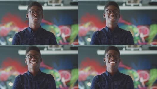 年轻黑人男性创造性地对着镜头微笑，在休闲办公室的壁画前，头和肩膀高清在线视频素材下载