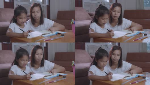 年轻的亚洲母亲在家里帮助她的女儿做家庭作业的慢动作。居家教育理念。高清在线视频素材下载