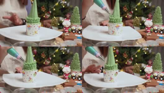 这是一个冬日传统节日准备烘焙食品和甜点架的特写镜头，自制纸杯蛋糕作为圣诞树，在装饰有圣诞老人和企鹅糖衣的桌子上添加绿色奶油作为树叶高清在线视频素材下载