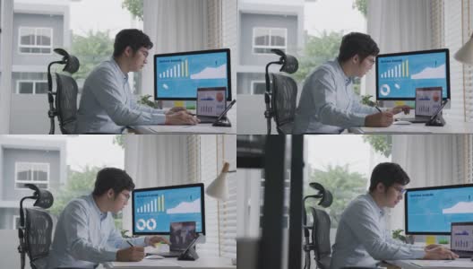 侧面的年轻迷人的亚洲泰国男子忙着工作的多屏幕电脑或智能平板电脑在桌子上在家里的自由职业者数据分析师，数据科学科学家的业务。高清在线视频素材下载