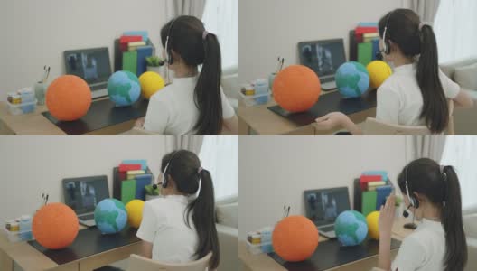一名亚洲少女通过客厅的笔记本电脑屏幕向老师在线展示她的科学作品，当时学校因COVID-19疫情而停课。高清在线视频素材下载