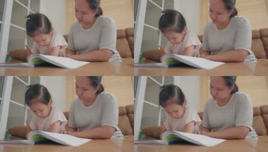 亚洲母亲照顾她的小女孩学习写在学校作业在家里高清在线视频素材下载