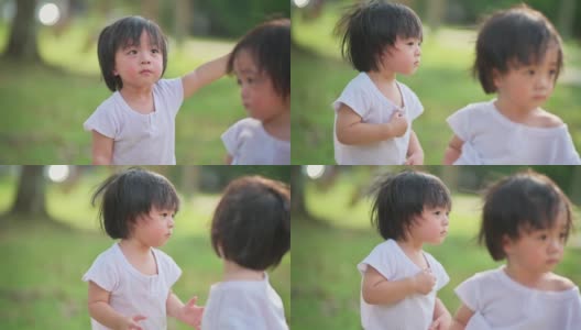 可爱的亚洲华人双胞胎男婴好奇地看着草坪公园里慢跑经过的人们高清在线视频素材下载