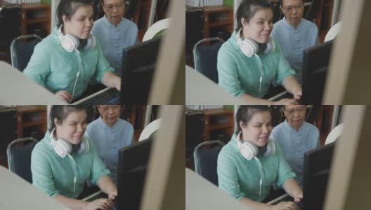 真实的盲人女性带着耳机使用电脑和盲文显示辅助装置与高级同事在工作场所讨论，手持拍摄。高清在线视频素材下载