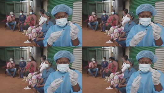 非洲黑人女护士从小瓶中提取Covid-19疫苗液体。非洲人在农村定居点排队接种Covid-19疫苗。高清在线视频素材下载