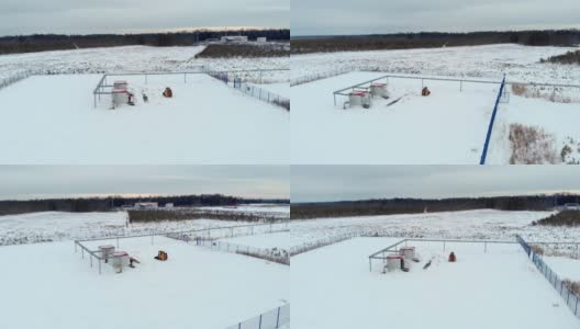 一架无人机飞过一个工业设施，一架小型拖拉机装载机清除该地区的积雪，以便工人进行正常的设备维护。北方国家的工业在零度以下高清在线视频素材下载