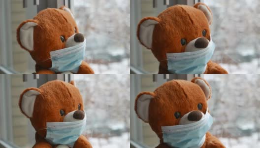 在新冠肺炎隔离期间，戴着防护口罩的好奇泰迪熊透过窗户看着外面的雪花高清在线视频素材下载