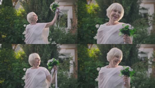 快乐的老女人站在阳光下，欣赏着新娘花束，微笑着看着镜头。现场镜头放大到美丽自信的白人新娘在户外享受婚礼的日子。高清在线视频素材下载