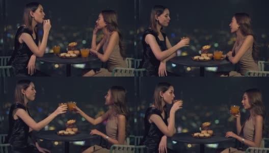 晚上，4K亚洲女性朋友在摩天大楼的屋顶餐厅吃晚餐，喝鸡尾酒。高清在线视频素材下载
