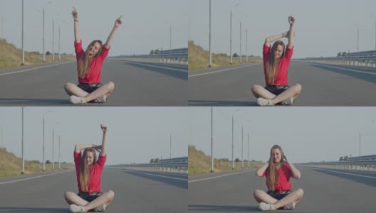一位年轻女子坐在柏油路上，高兴地举起双手。高清在线视频素材下载
