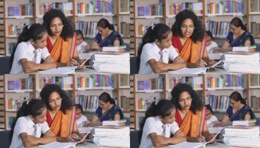 在图书馆帮助女学生学习的老师高清在线视频素材下载