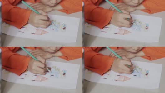 穿着橙色衬衫的小男孩正在纸上画画。高清在线视频素材下载